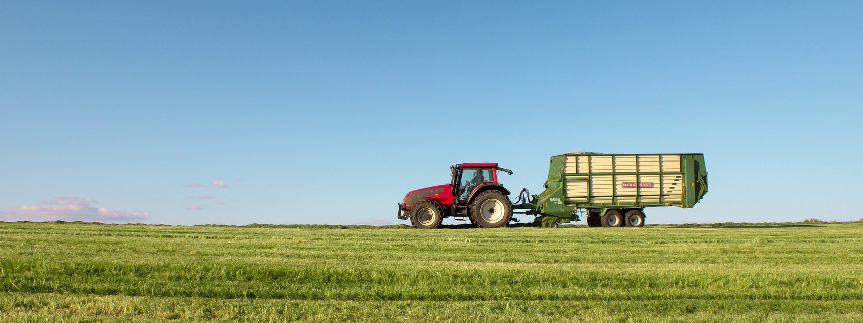 Traktor mit Anhänger fährt über eine Wiese
