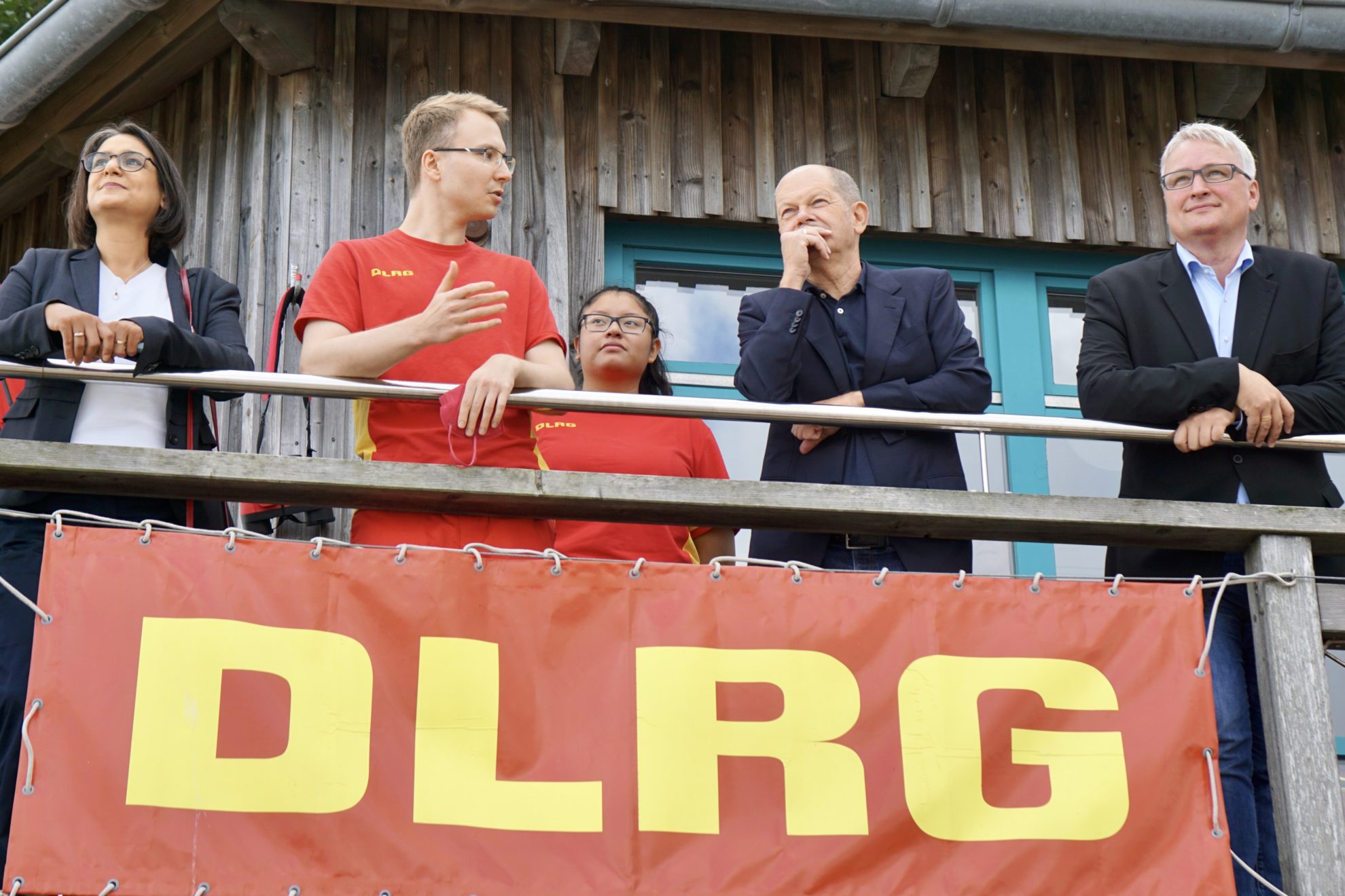 Serpil Midyatli, Olaf Scholz und Sönke Rix stehen beim DLRG auf dem Balkon und lassen sich die Funktionsweise des DLRG erklären.